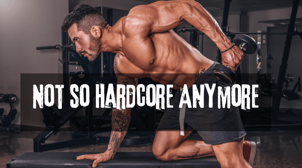 male-presenting shirtless weightlifter holding dumbbell. kneeling with one knee on a weight bench. text reads: not so hardcore anymore. 